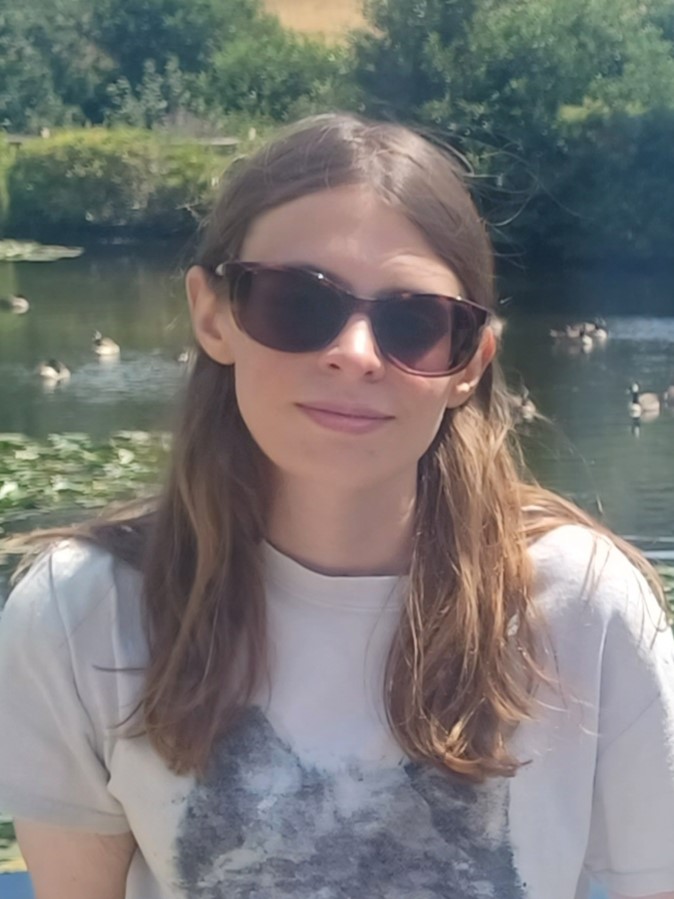 Image of Lauren Eade, East Sussex SLC member. Lauren is sitting in a garden in the sun. She has long, brown, hair and is wearing sunglasses.