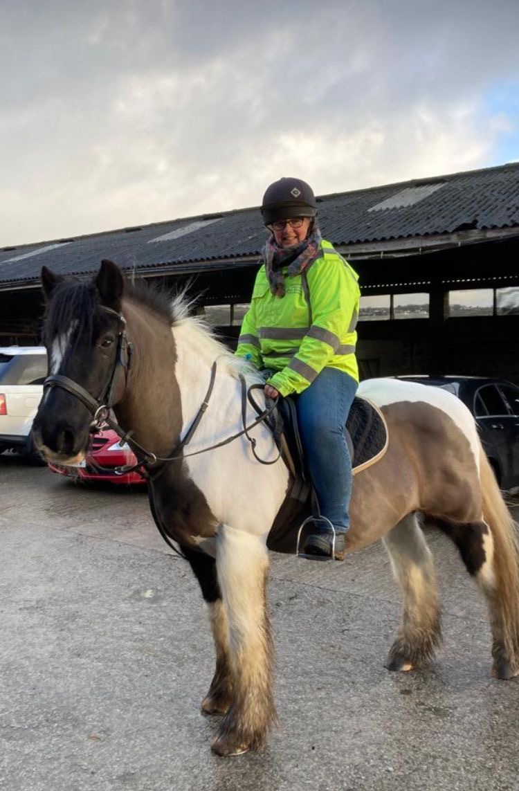 Allison David, Lancashire SLC member, pictured sitting on her horse, Ted, a brown and white cob. Allison is wearing a high vis jacket, and smiling at the camera.