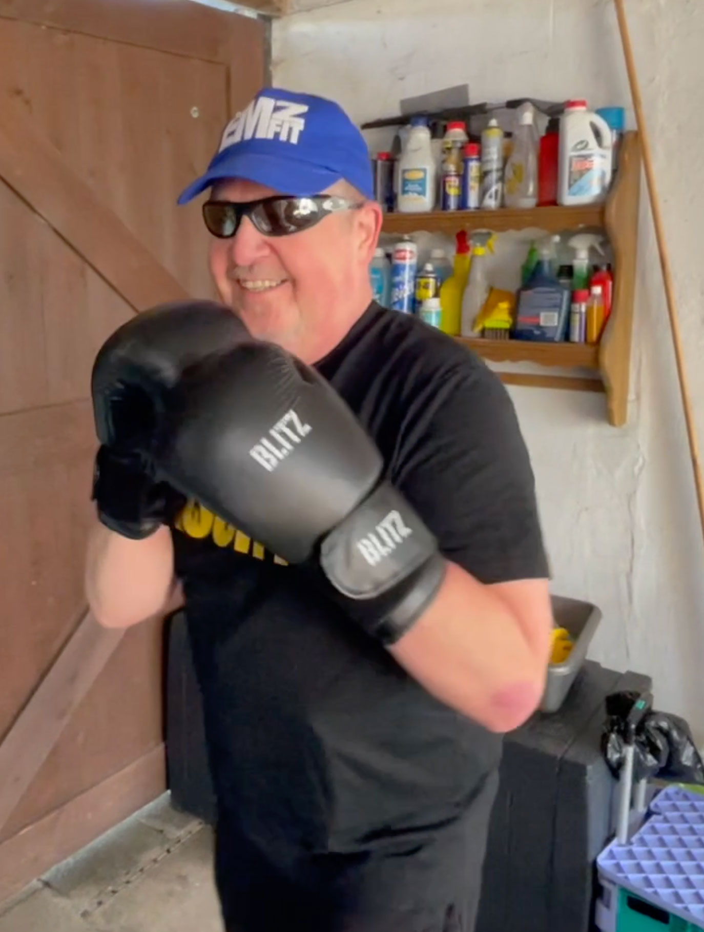James Connell, Merseyside SLC member, holding his arms up in a sparring pose. He is wearing black boxing gloves, sunglasses, and a blue baseball hat and is smiling towards the camera.