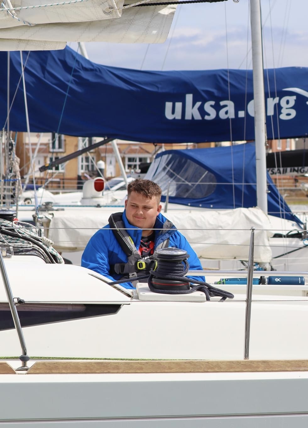 Lloyd Sakr, Lancashire SLC member, pictured on a sail boat, sitting under the sail. He is wearing a blue jacket and black life jacket.