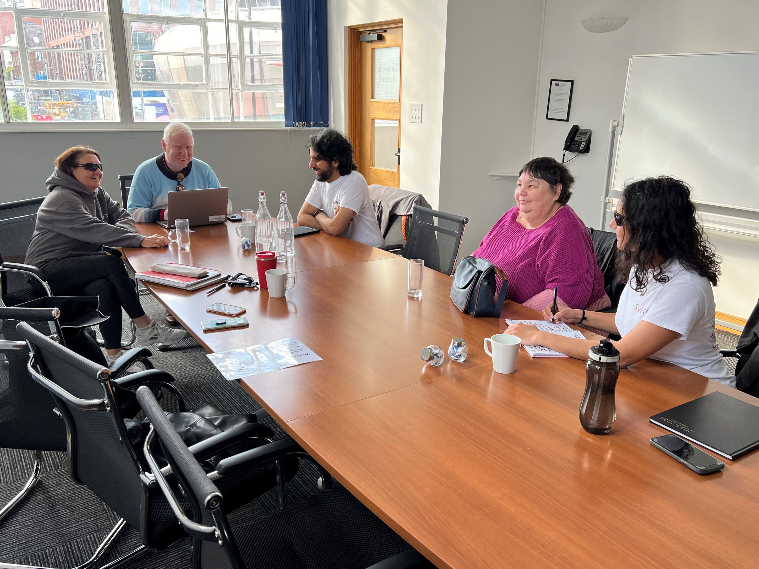 South Yorkshire SLC members sat around a board room table during their first face-to-face meeting. From left to right: Janiece, Iain Mitchell, Senior Engagement Manager for North England, Ameen, Helen, and Parv. They are in mid-conversation.