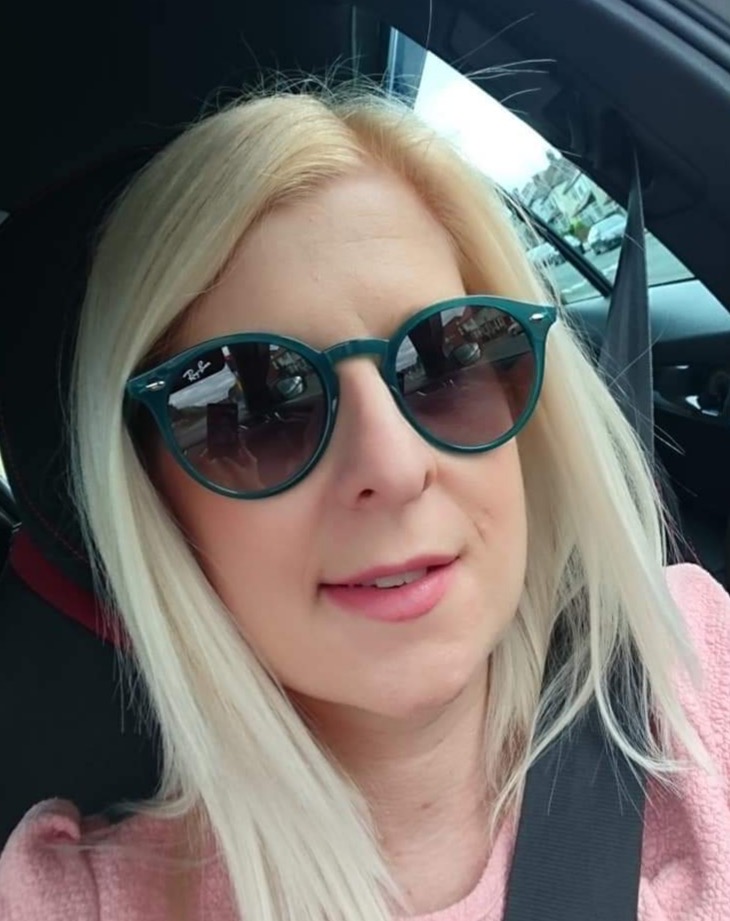 Headshot of Louise Connop. She is sat in a car, wearing sunglasses and smiling at the camera