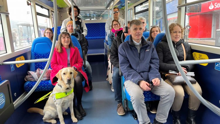 [8 people, including SLC staff members and volunteers sitting on a bus with blue seats and smiling at the camera.]