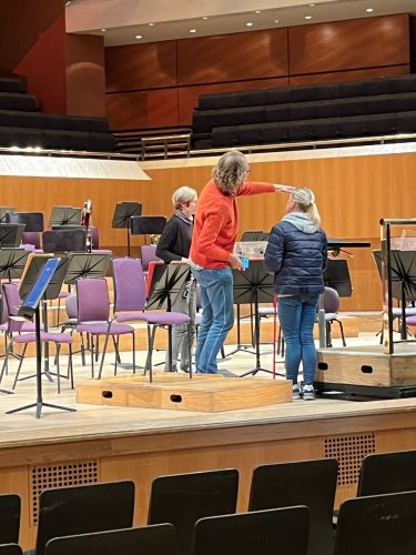 Kelly Barton standing in orchestra pit talking to Halle Orchestra members 