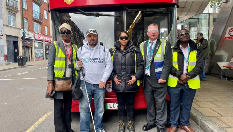 London SLC Volunteer, Steve Reed, standing in front of a red bus with four TFL bus drivers and trainers at a Meet The Bus event in London