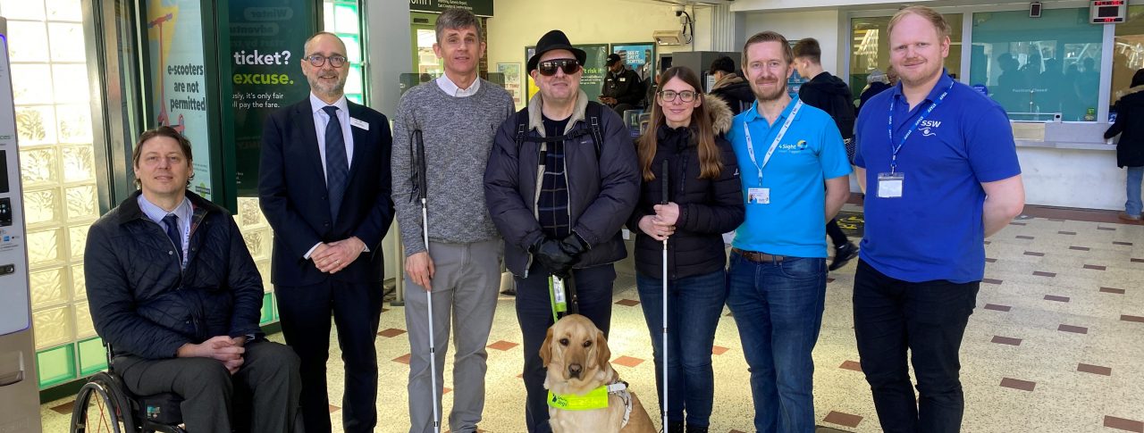 From left to right: Carl Martin, Accessibility Lead at GTR, Dave Smith, Engagement Manager for South East England, Paull Goddard, East Sussex SLC member, Lauren Eade, SLC coordinator, with staff members from GTR. They are stood together in a line in the ticket hall at Chichester Station.