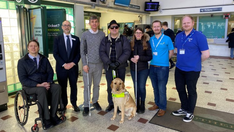 From left to right: Carl Martin, Accessibility Lead at GTR, Dave Smith, Engagement Manager for South East England, Paull Goddard, East Sussex SLC member, Lauren Eade, SLC coordinator, with staff members from GTR. They are stood together in a line in the ticket hall at Chichester Station.