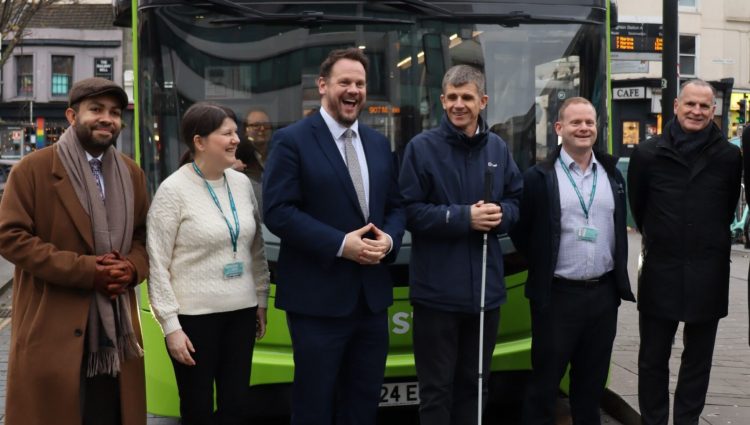 Dave stood with Transport Minister Simon Lightwood, Victoria Garcia, Ed Wills and another outside of Coaster bus at a bus stop. They are stood infront of the bus and smiling a the camera. The green bus says 'Accessible Travel' and the words 'Stephen Barnwell' at the top.