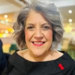 Helen Murphy is smiling at the camera. Helen has grey curly hair and is wearing a black top.