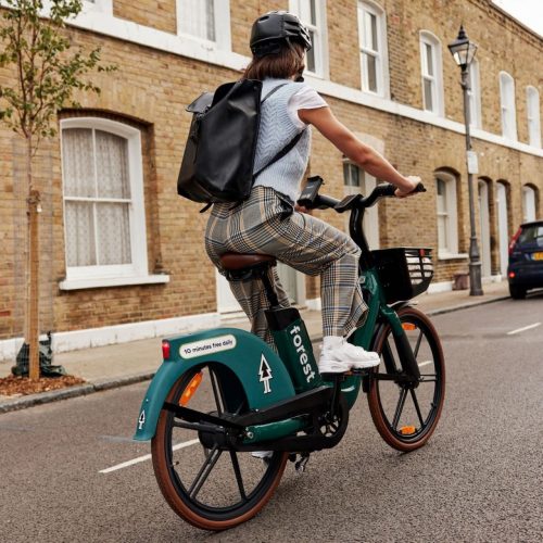 A woman riding a Forest bike. She is wearing a white t-shirt, grey tartan trousers as well as a black backpack and black helmet.