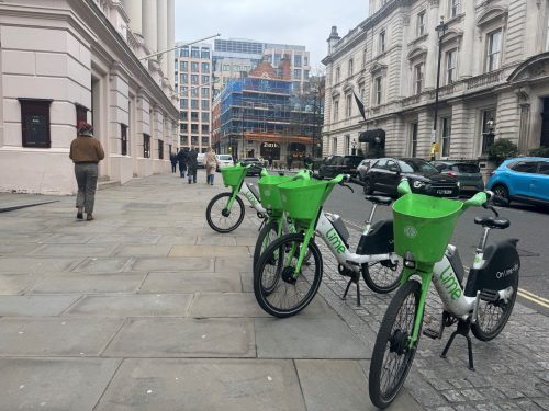 Row of Lime bikes parked on a pavement.